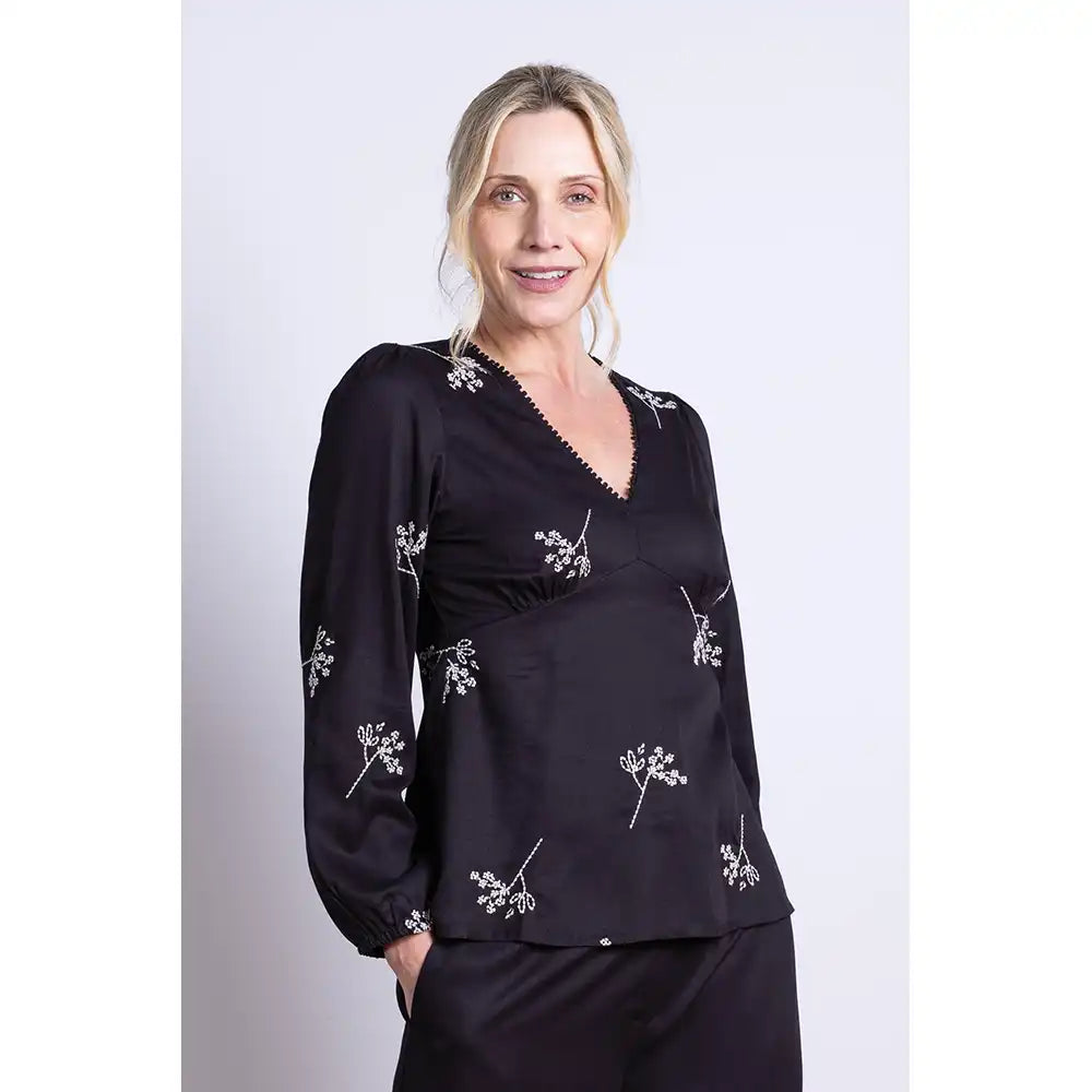 Woman wearing a black blouse with white floral patterns on a plain background