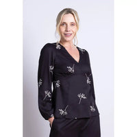 Woman wearing a black blouse with white floral patterns on a plain background