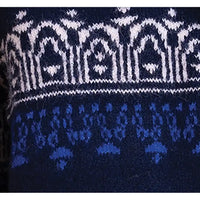 Close-up of a knitted textile with a white geometric pattern band above a blue patterned section on a dark navy background.