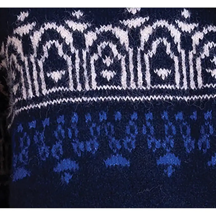 Close-up of a knitted textile with a white geometric pattern band above a blue patterned section on a dark navy background.