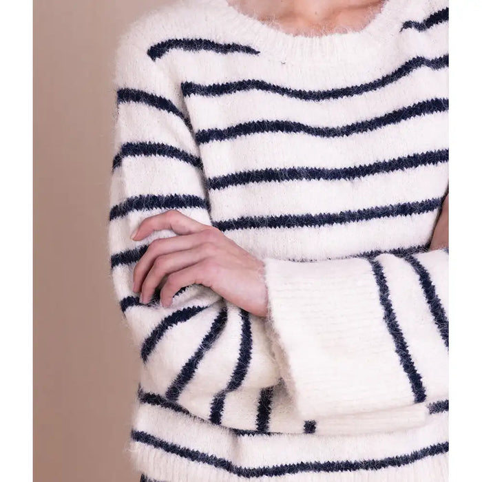 A close-up of a person wearing a fuzzy knit sweater with horizontal navy blue stripes on an off-white base, cropped from the neck to the hips against a plain beige background.