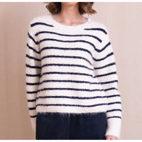 A person wearing a fuzzy knit sweater with horizontal navy blue stripes on an off-white background, paired with dark corduroy pants, against a plain beige wall.