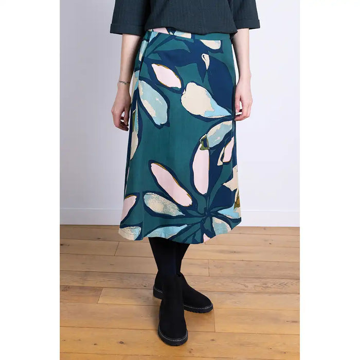 Person wearing a patterned skirt in teal, navy and multi colours with a plain background