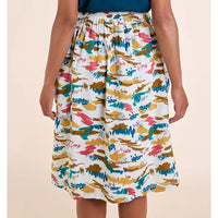A model wearing a white A-line midi skirt with a colorful abstract brushstroke pattern in teal, mustard yellow, pink, and brown, paired with a dark blue top against a solid beige background.
