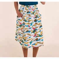 A model wearing a white midi skirt with a colorful abstract brushstroke pattern in blue, pink, and mustard yellow, featuring side pockets.