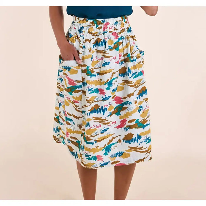 A model wearing a white midi skirt with a colorful abstract brushstroke pattern in blue, pink, and mustard yellow, featuring side pockets.