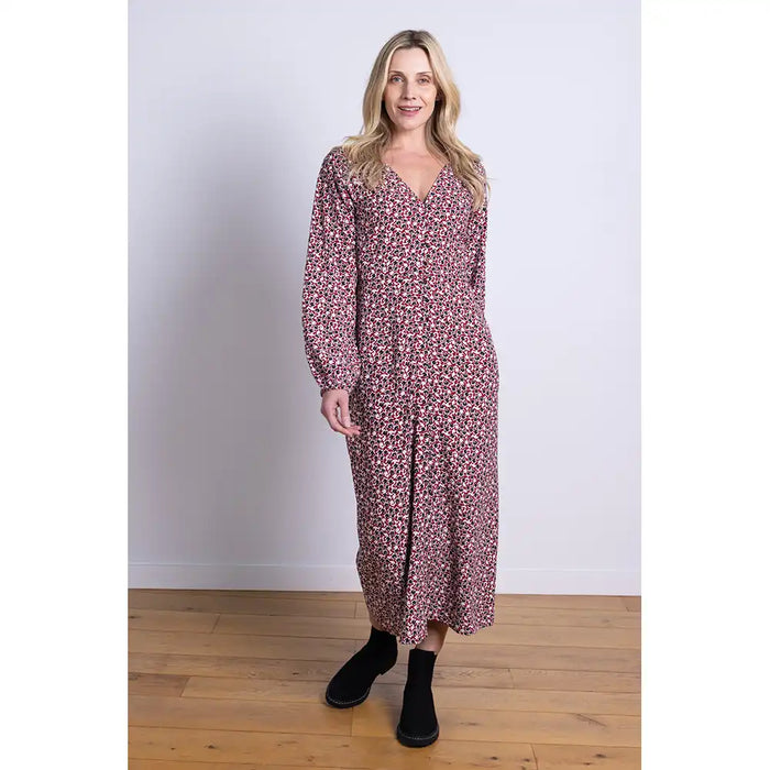 Woman wearing a floral midi dress wotu V neck and buttoned front, standing on a wooden floor with a white wall background