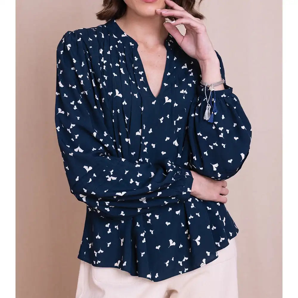 A woman wearing a navy blue long-sleeve blouse with a white butterfly print, paired with light beige pants, set against a solid beige background.