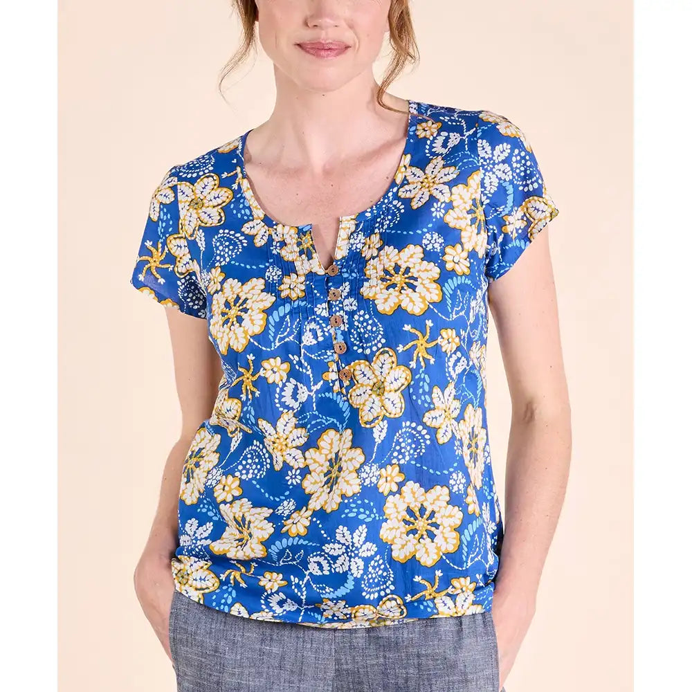 Bright blue top with short sleeves and round neckline. Neckline has a v notch in with and 5 brown buttons. White and yellow flowers printed on top. 