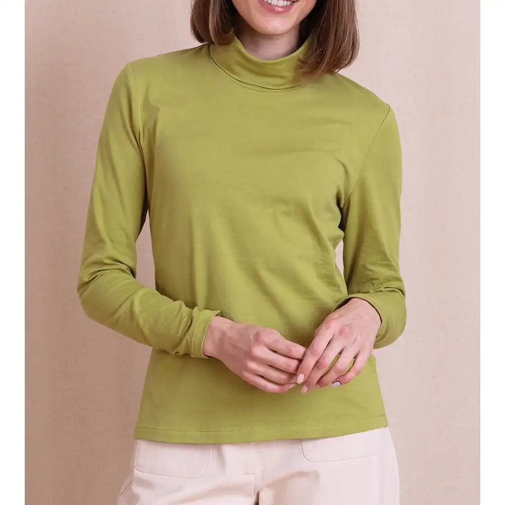A woman wearing a solid olive green mock neck long-sleeve top, paired with light beige pants, standing against a solid beige background.