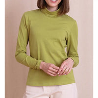 A woman wearing a solid olive green mock neck long-sleeve top, paired with light beige pants, standing against a solid beige background.