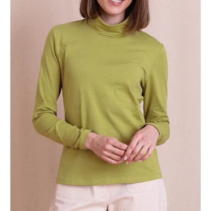 A woman wearing a solid olive green mock neck long-sleeve top, paired with light beige pants, standing against a solid beige background.