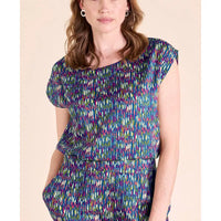 A woman wearing a colorful abstract-patterned short-sleeve top and matching bottoms against a plain beige background.