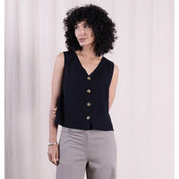 Woman wearing a black sleeveless top with gold buttons against a light background