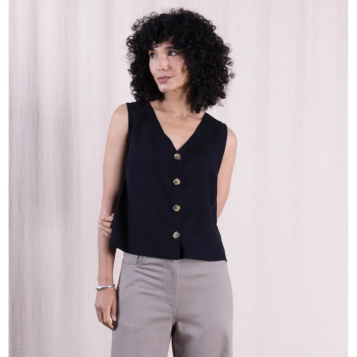 Woman wearing a black sleeveless top with gold buttons against a light background