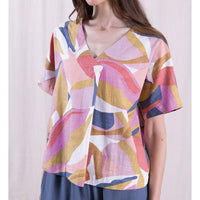 Woman wearing a colorful abstract patterned top against a plain background