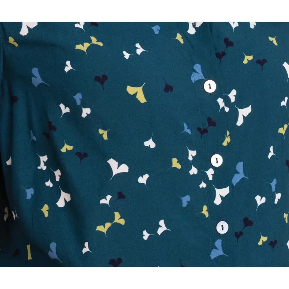 A close-up of a dark teal fabric with a repeating pattern of small ginkgo leaves in white, light blue, yellow, and dark navy, accented by two white buttons.