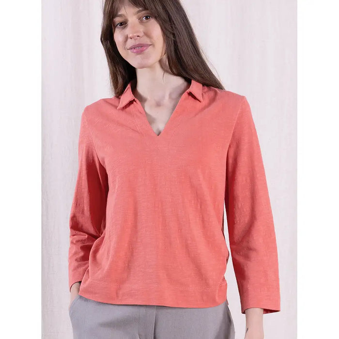 Woman wearing a coral long-sleeve shirt against a white background