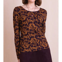 A woman wearing a long-sleeve knit top with an abstract floral pattern in dark brown and deep purple, paired with a dark purple ribbed skirt against a solid beige background.