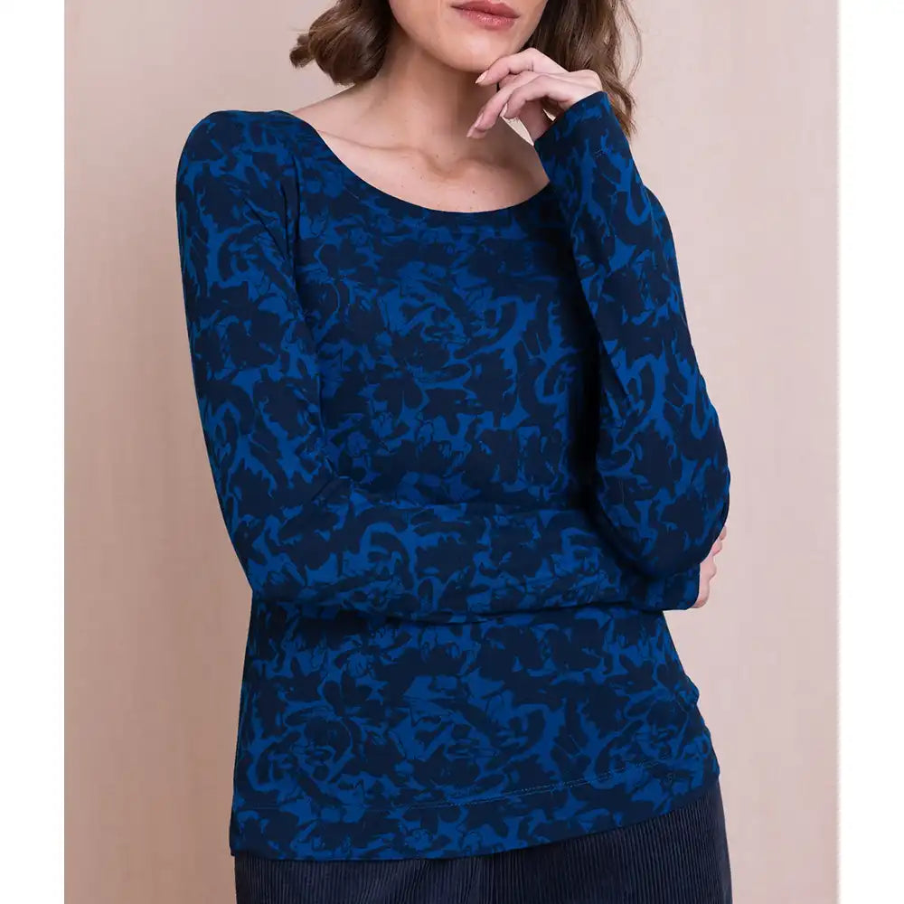 A woman wearing a long-sleeve scoop-neck top with an abstract blue and navy pattern, posed against a solid beige background.