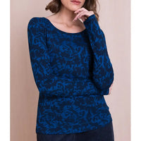 A woman wearing a long-sleeve scoop-neck top with an abstract blue and navy pattern, posed against a solid beige background.