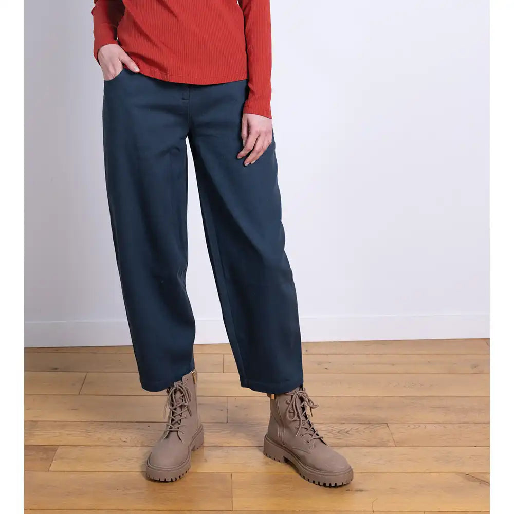 Person wearing navy pants and brown boots on a wooden floor with a white wall background