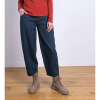 Person wearing navy pants and brown boots on a wooden floor with a white wall background