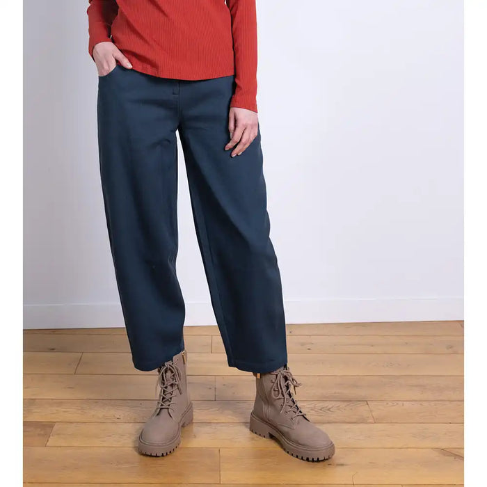 Person wearing navy pants and brown boots on a wooden floor with a white wall background