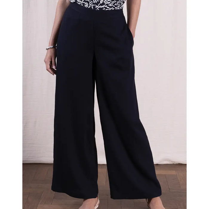 Person wearing black wide-leg pants with a white patterned top against a neutral background