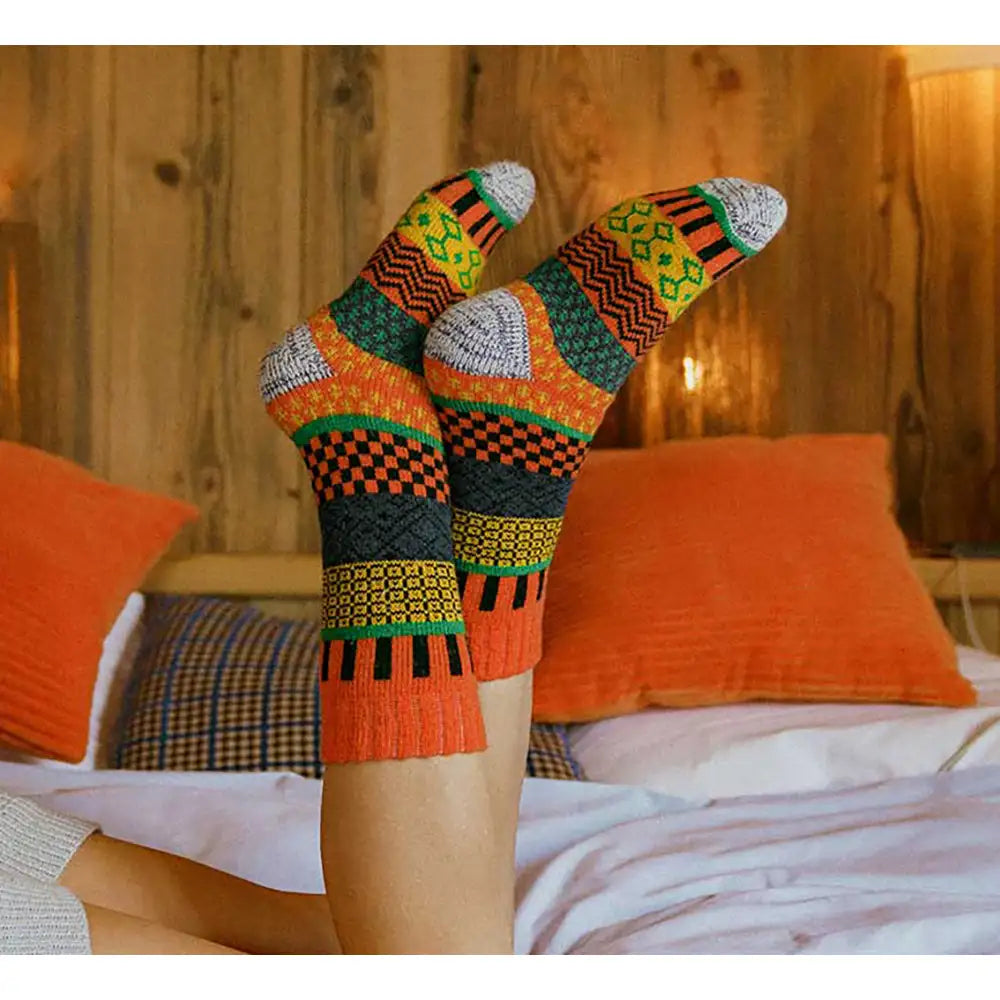 Colorful patterned socks worn by a person on a bed with orange pillows.