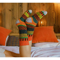 Colorful patterned socks worn by a person on a bed with orange pillows.
