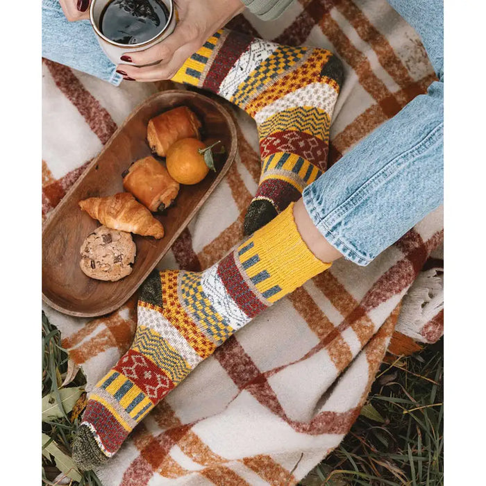 Person wearing patterned socks on a blanket with a tray of food and a cup.