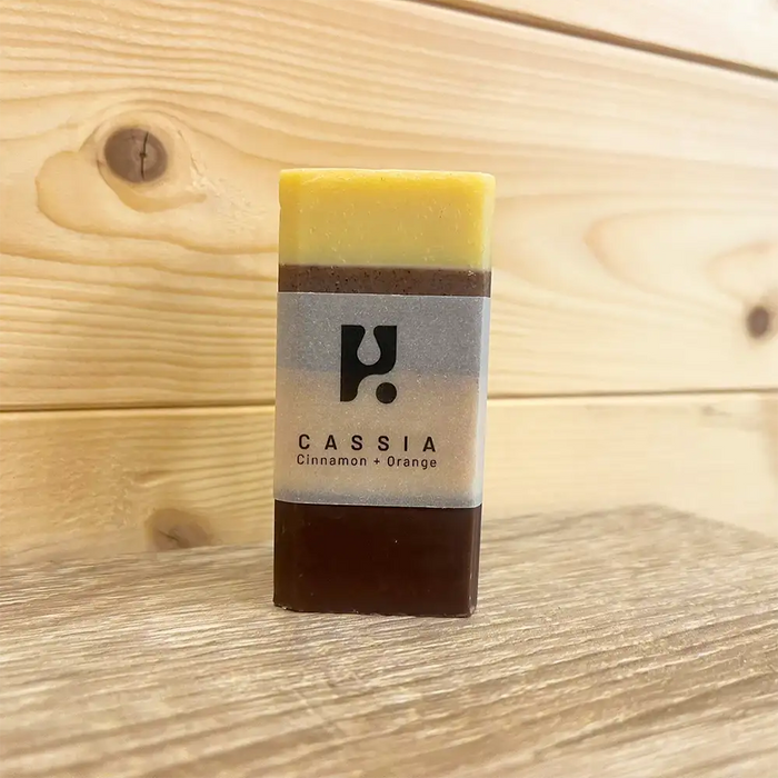 Rectangle bar of soap with an opaque band round it with black. Writing states 'Cassia cinnamon and orange'. Soap has four colours in horizontal bands. 