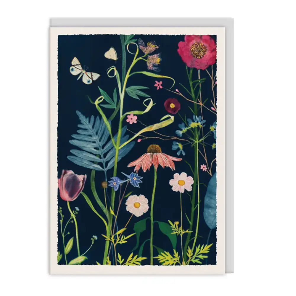 A vertical art print or greeting card featuring a botanical illustration with wildflowers, leaves, and butterflies on a dark navy background, shown against a plain white studio backdrop.