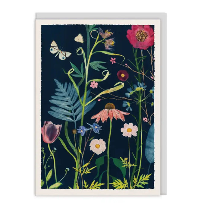 A vertical art print or greeting card featuring a botanical illustration with wildflowers, leaves, and butterflies on a dark navy background, shown against a plain white studio backdrop.