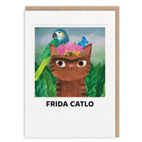 A greeting card featuring a whimsical illustration of a brown cat with a pink flower crown and a green parrot on its back, with the text 'FRIDA CATLO' below. The card has a white border and is shown with a brown kraft envelope behind it on a white background.