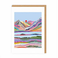 A vertical art print or greeting card featuring a colorful stylized landscape with mountains, fields, and a red sun, shown with a kraft paper envelope behind it on a white background.