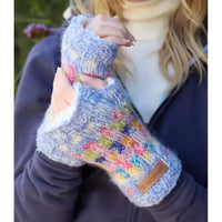 Colorful knitted mittens with a brand label held by a person outdoors.