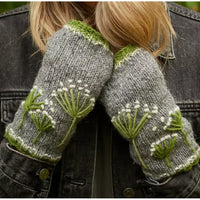A close-up of a person wearing gray knit fingerless gloves with green and white dandelion embroidery, shown against a dark denim jacket.