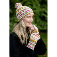 A woman wearing a colorful knit beanie with a pom-pom and matching fingerless gloves, posed outdoors against a blurred green background.