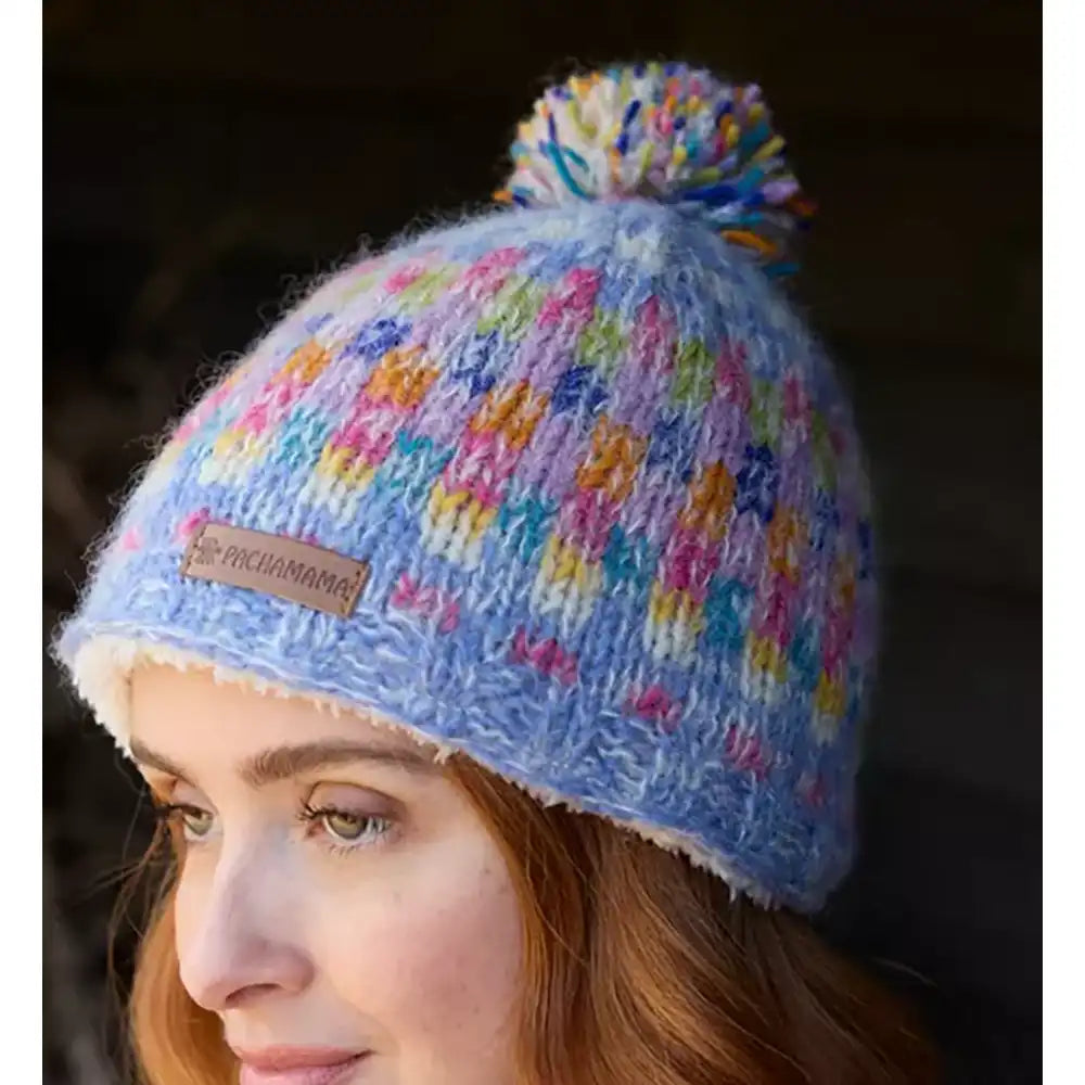 Colorful knitted beanie with pom-pom worn by a person, featuring a visible brand label.