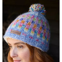 Colorful knitted beanie with pom-pom worn by a person, featuring a visible brand label.
