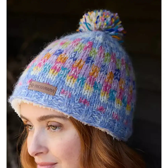 Colorful knitted beanie with pom-pom worn by a person, featuring a visible brand label.