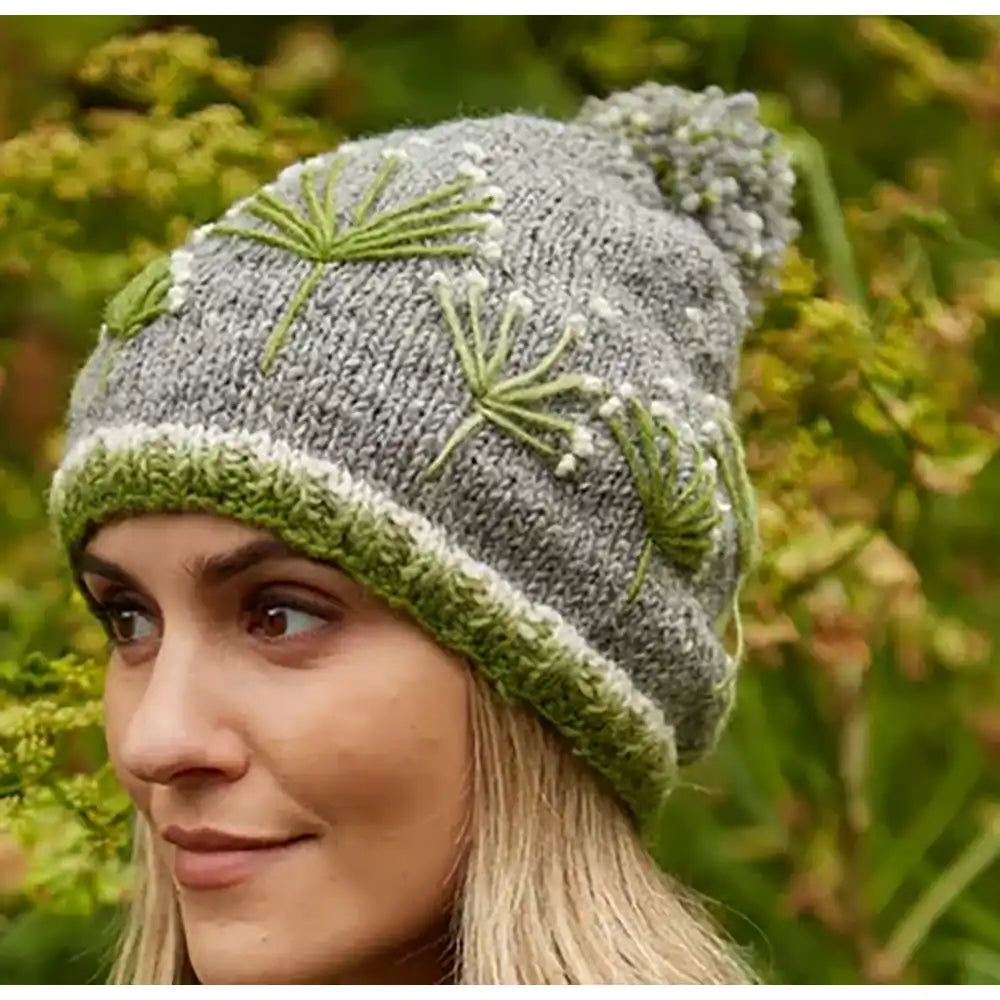Woman wearing a gray knit hat with green floral patterns against a natural background