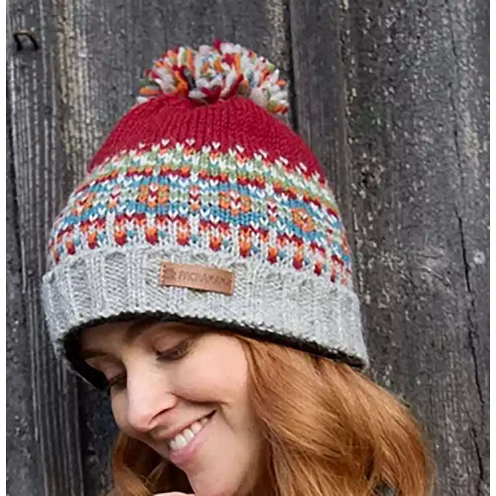 Person wearing a colorful knitted beanie with a brand label against a wooden background