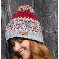 Person wearing a colorful knitted beanie with a brand label against a wooden background