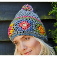 Woman wearing a colorful crocheted beanie with floral patterns against a dark background.