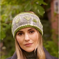 A woman wearing a gray headband with green and white leaf patterns, photographed outdoors against a blurred green foliage background.