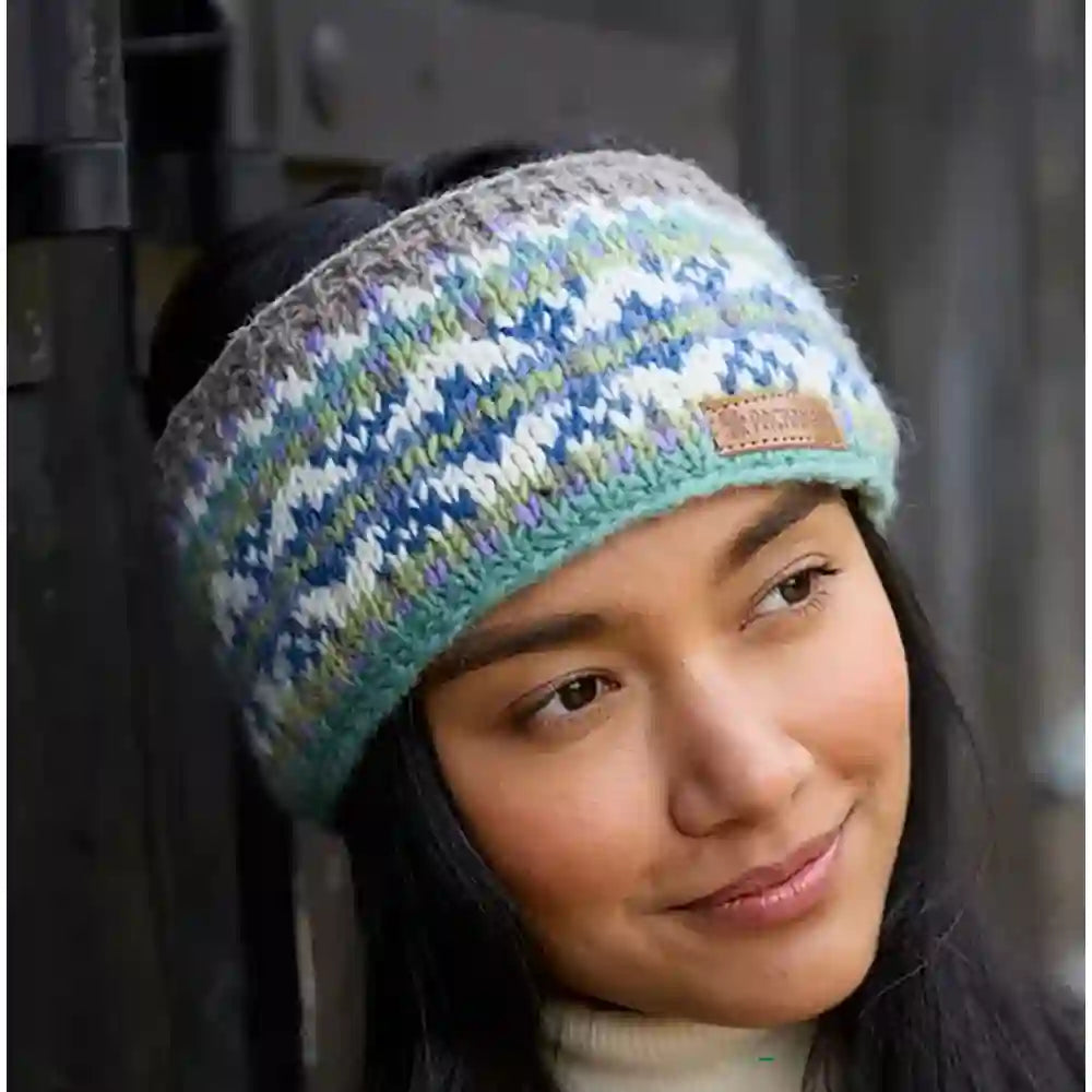 A woman wearing a knitted headband with a blue, green, and white geometric pattern and a small tan brand patch on the side.