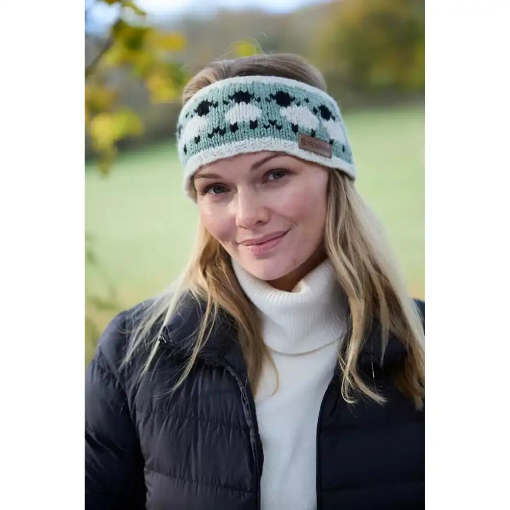 Woman wearing a woollen headband with white and black sheep on a green background.